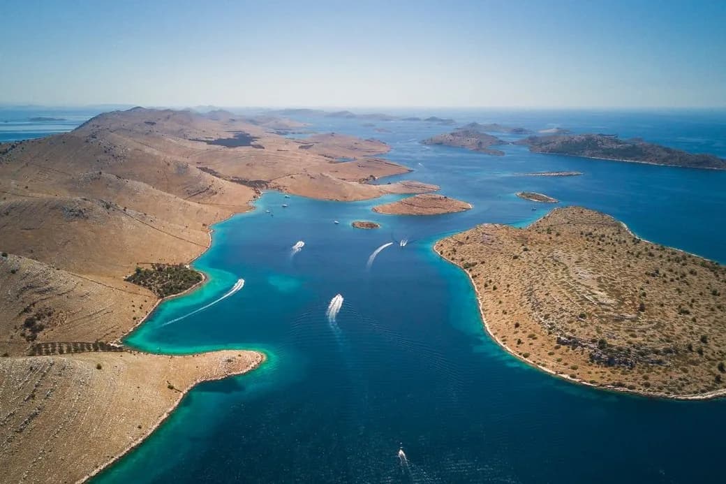 Vue aérienne des îles nues et rocailleuses de l'archipel des Kornati, avec un chenal turquoise et des bateaux