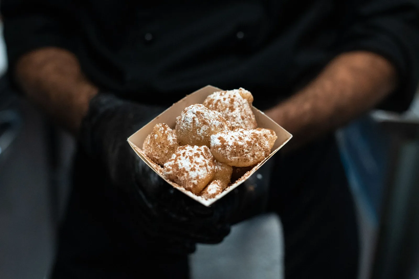 Cornet de petits beignets ronds saupoudrés de sucre glace, tenu à deux mains