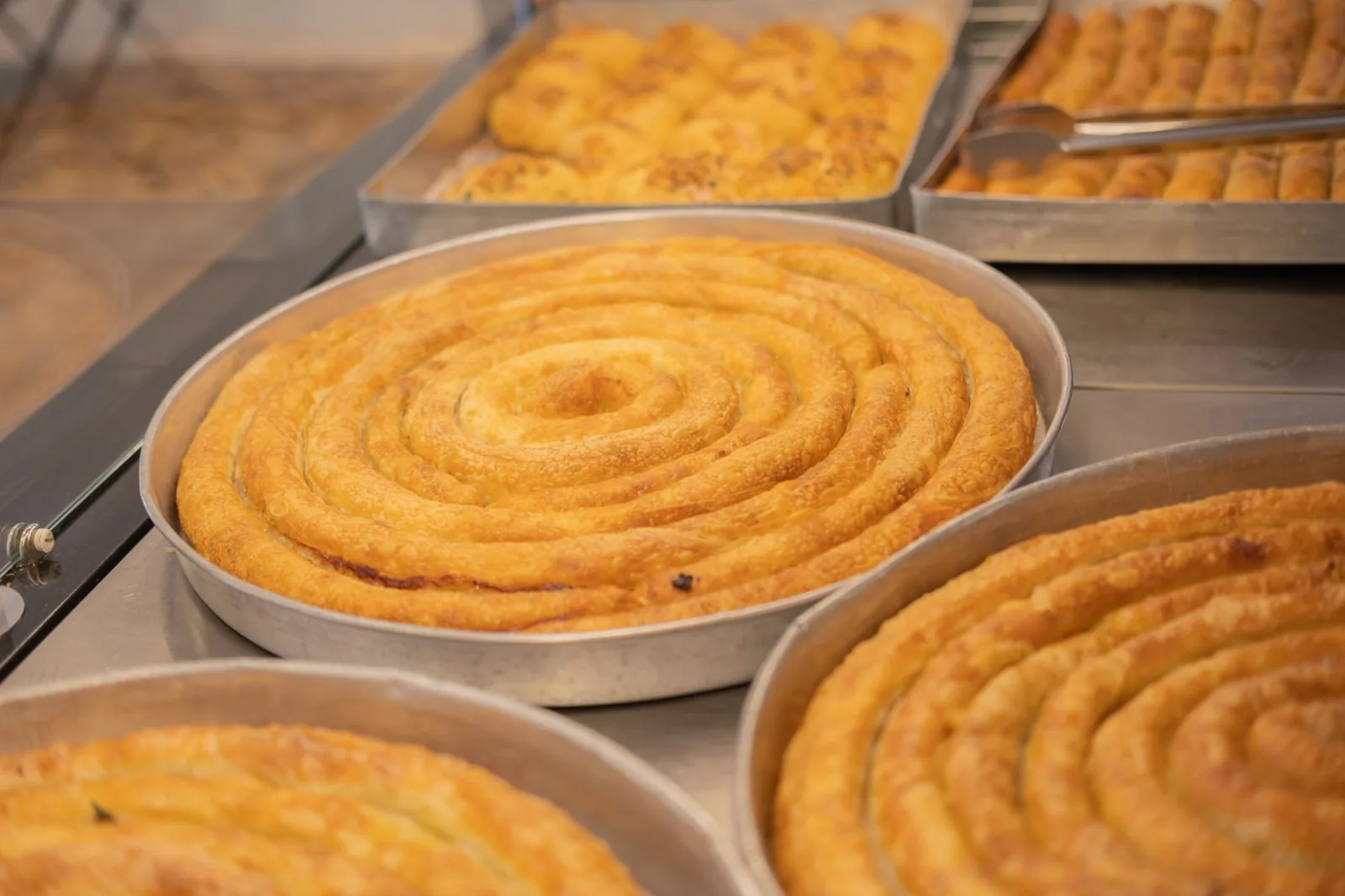 Des bureks en spirale, feuilletés et dorés, dans de grands plats en métal chez un boulanger
