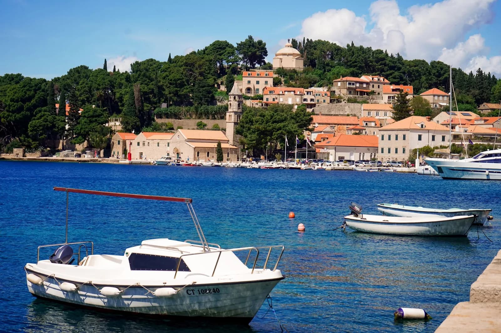 Bateaux amarrés dans le port de Cavtat devant les maisons en pierre à toits orange et la pinède