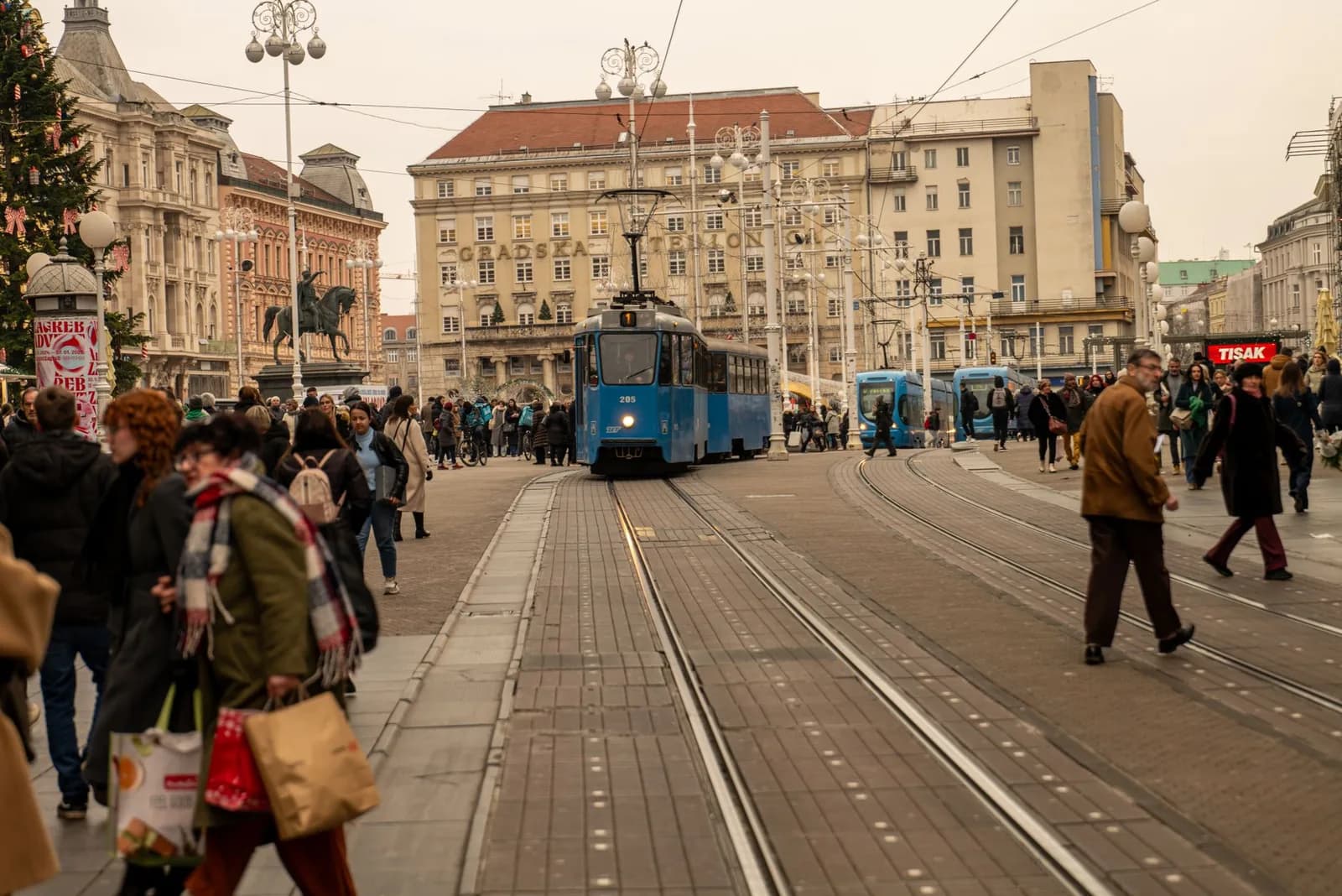 Tramway bleu et foule de passants dans le centre de Zagreb, en fin de journée à l'approche de Noël