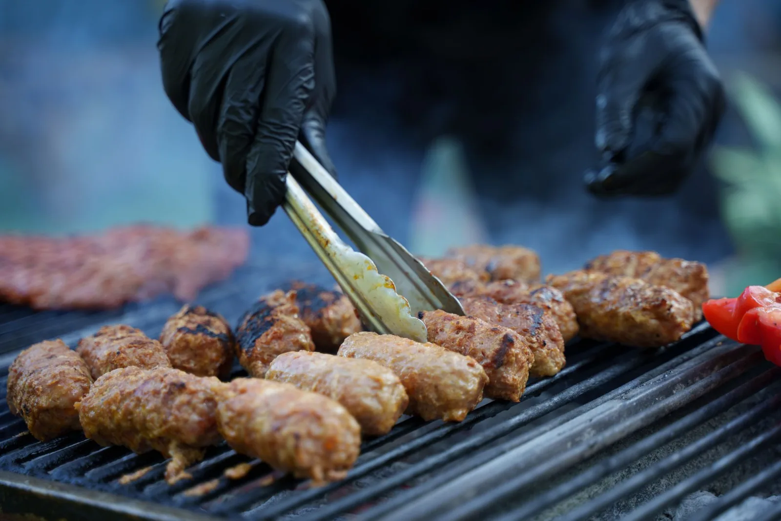 Des ćevapi grillés retournés à la pince sur un gril