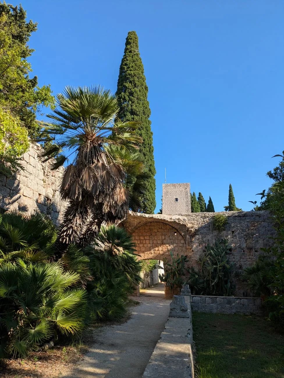 Cour de monastère en pierre avec palmiers, cyprès et arche, sur la côte dalmate
