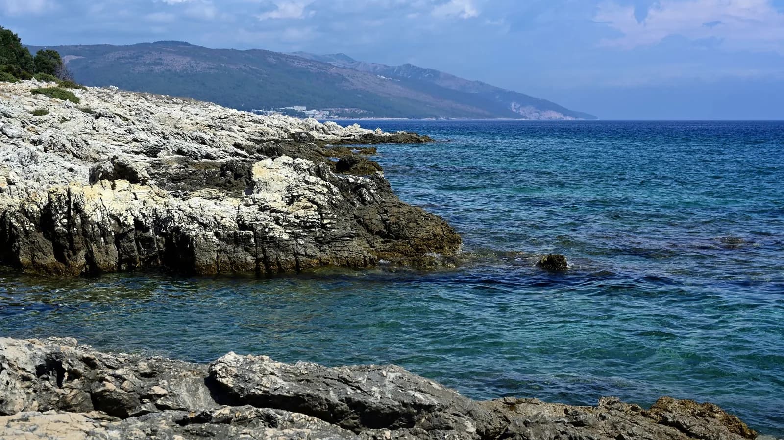Côte rocheuse déserte et eau bleue de l'Adriatique, avec des collines au fond