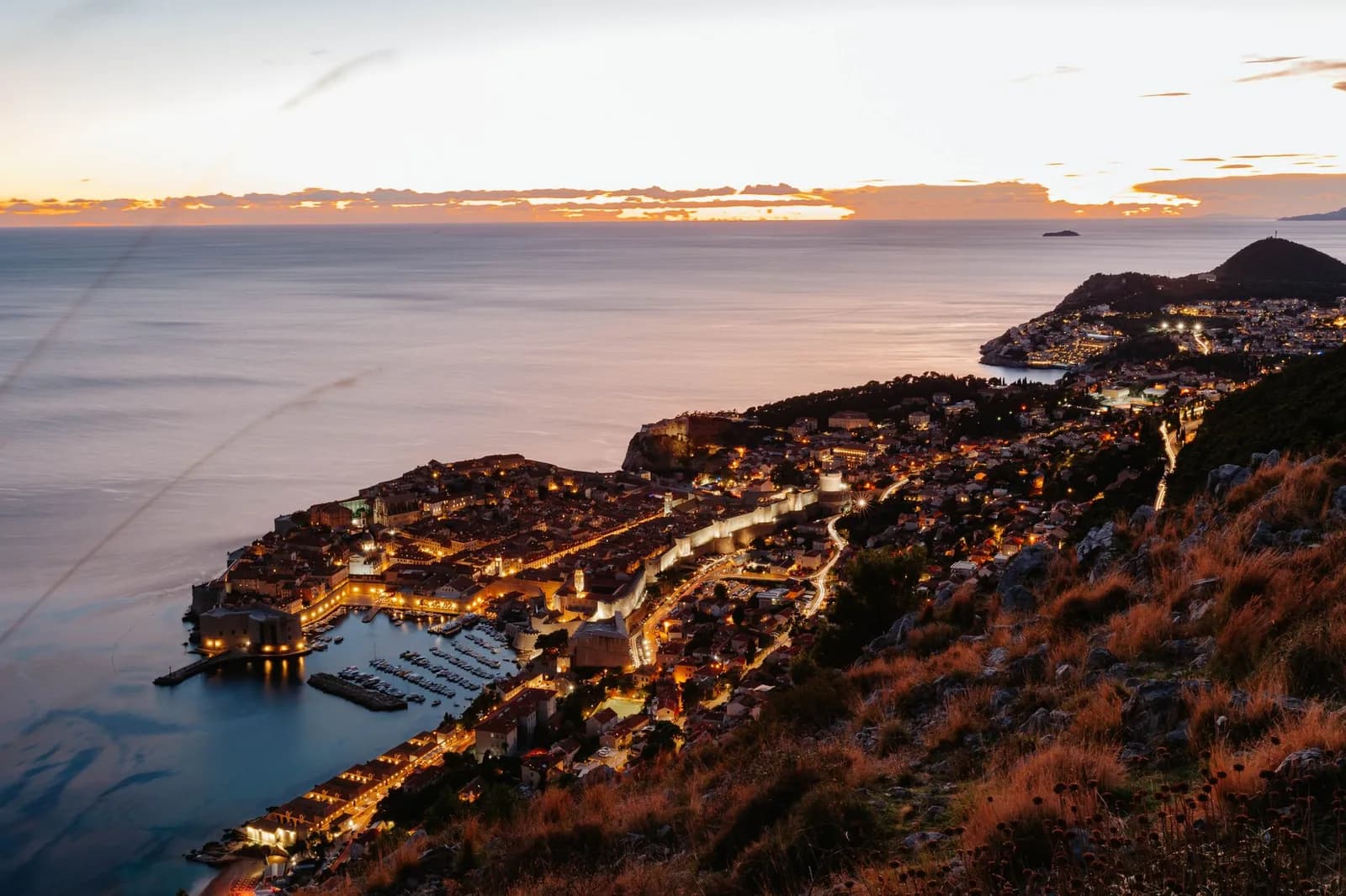 La vieille ville de Dubrovnik illuminée au crépuscule, vue depuis le mont Srđ, avec l'Adriatique à l'horizon