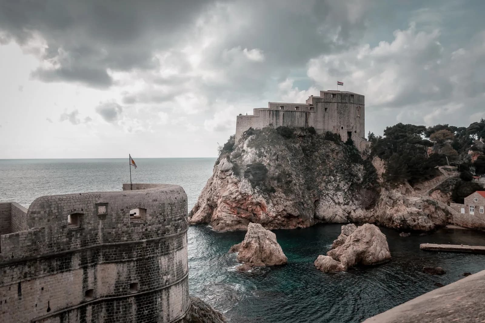 Remparts de Dubrovnik au premier plan et fort Lovrijenac sur son rocher au-dessus de l'Adriatique, sous un ciel nuageux