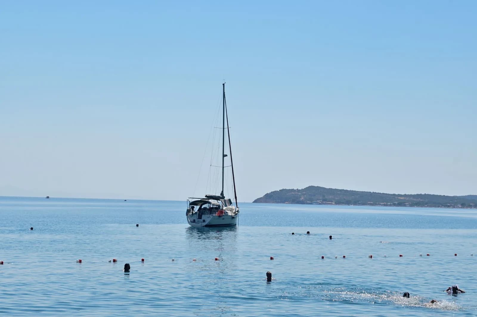 Baigneurs dans une mer calme et claire autour d'un voilier au mouillage