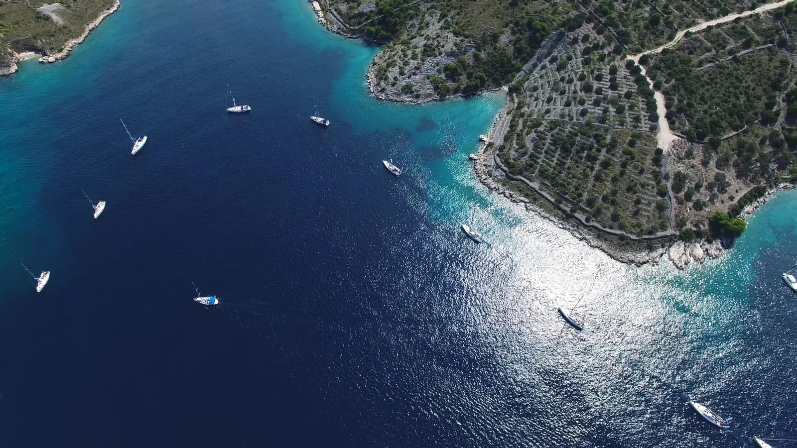 Vue aérienne de voiliers au mouillage dans une baie aux eaux turquoise, devant une côte rocheuse en terrasses