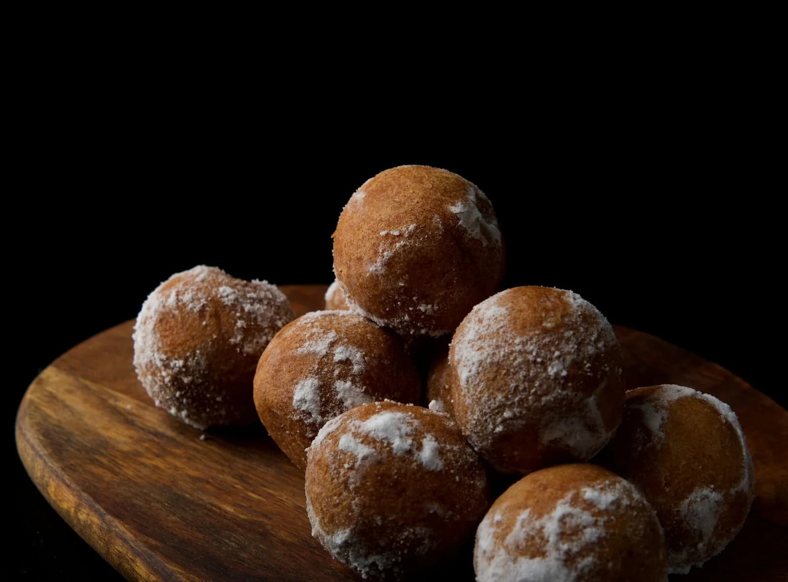 Des petits beignets ronds saupoudrés de sucre, posés sur une planche en bois