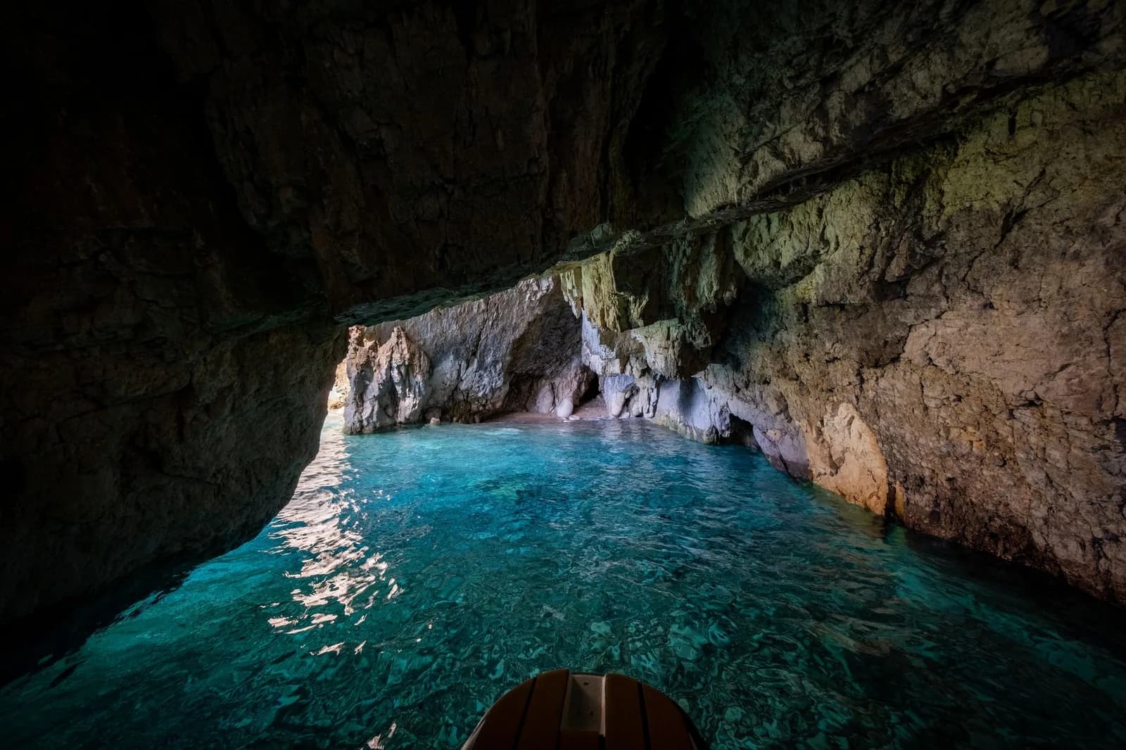 Intérieur d'une grotte marine aux eaux turquoise, vu depuis la proue d'une barque