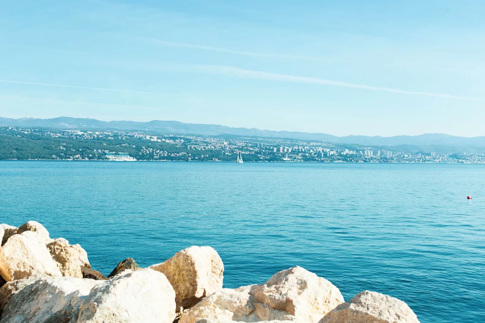 Rochers clairs au bord d'une mer bleue sur la côte du Kvarner, avec Rijeka au loin