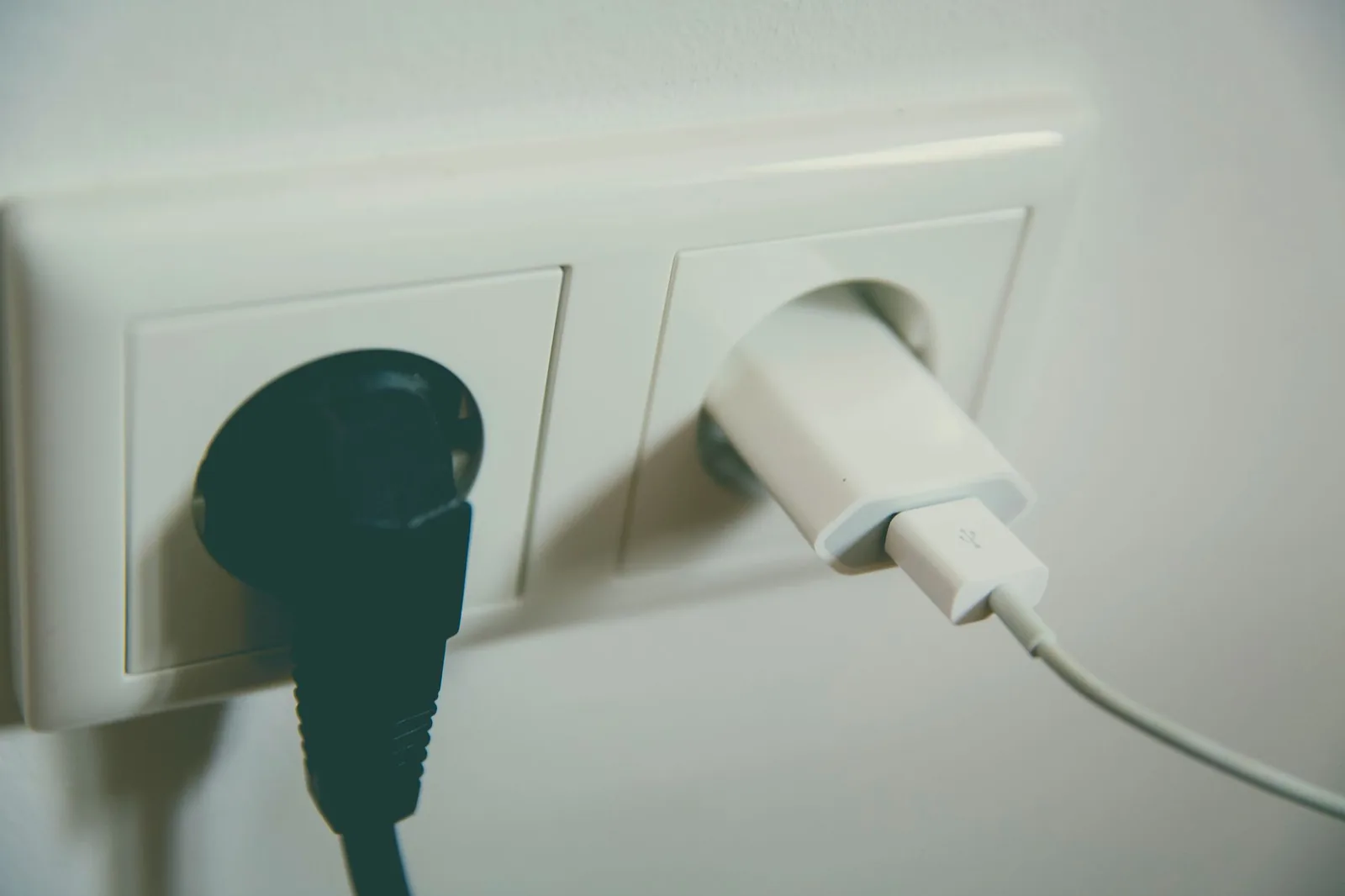 Gros plan d'une double prise murale de type F avec une fiche noire et un chargeur USB blanc branchés