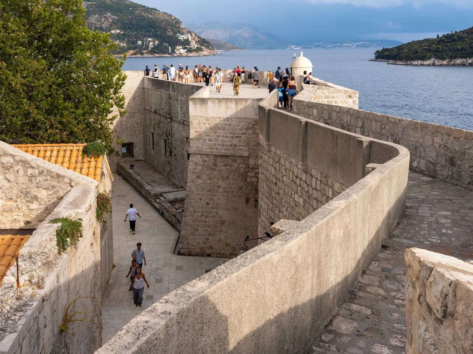Promeneurs sur le chemin de ronde des remparts de Dubrovnik, avec l'Adriatique et l'île de Lokrum au loin