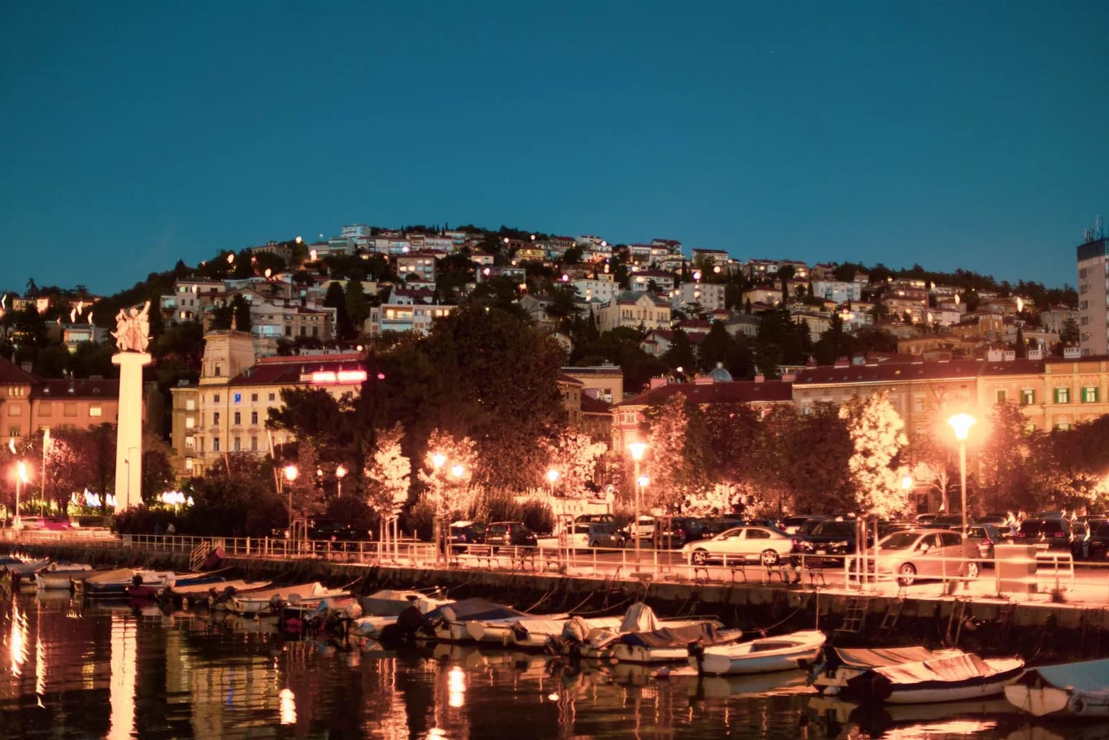 Le port de Rijeka et ses bateaux le soir, avec les maisons illuminées sur la colline