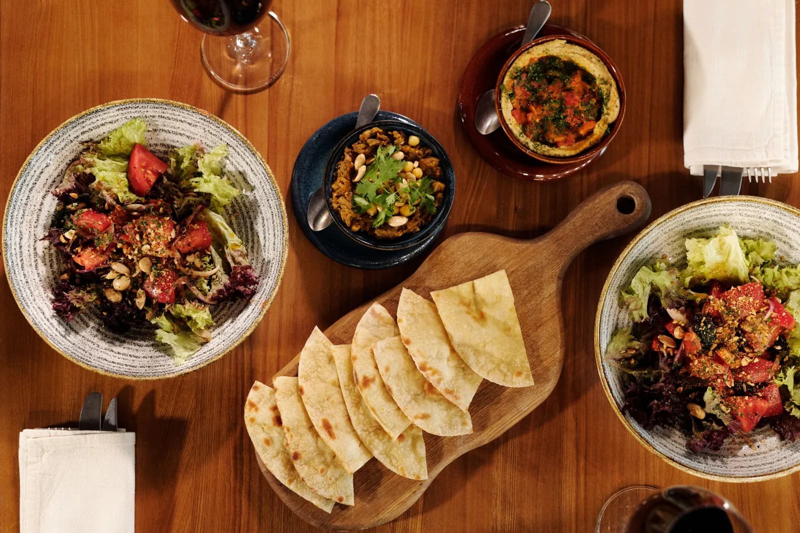 Une table en bois avec salades, pain plat et vin à partager