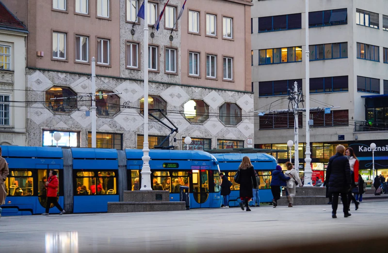 Un tramway bleu et des passants en manteau sur une place du centre de Zagreb, en Croatie