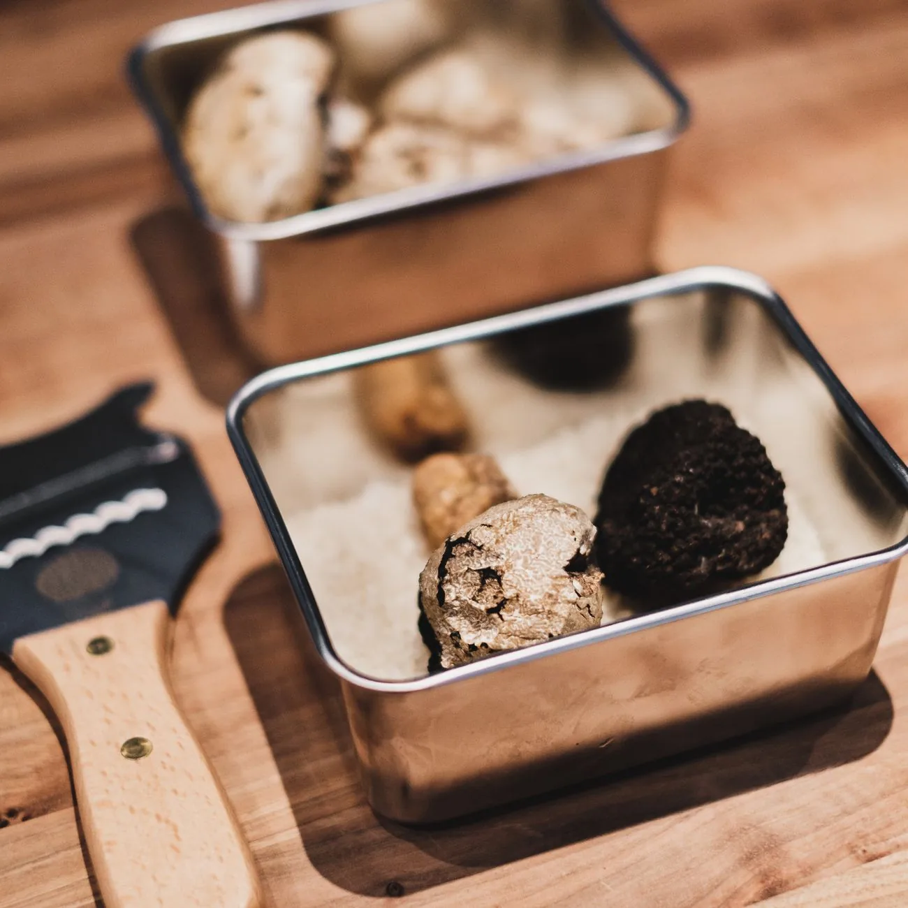 Des truffes dans des boîtes en métal, avec une râpe à truffe, sur une table en bois
